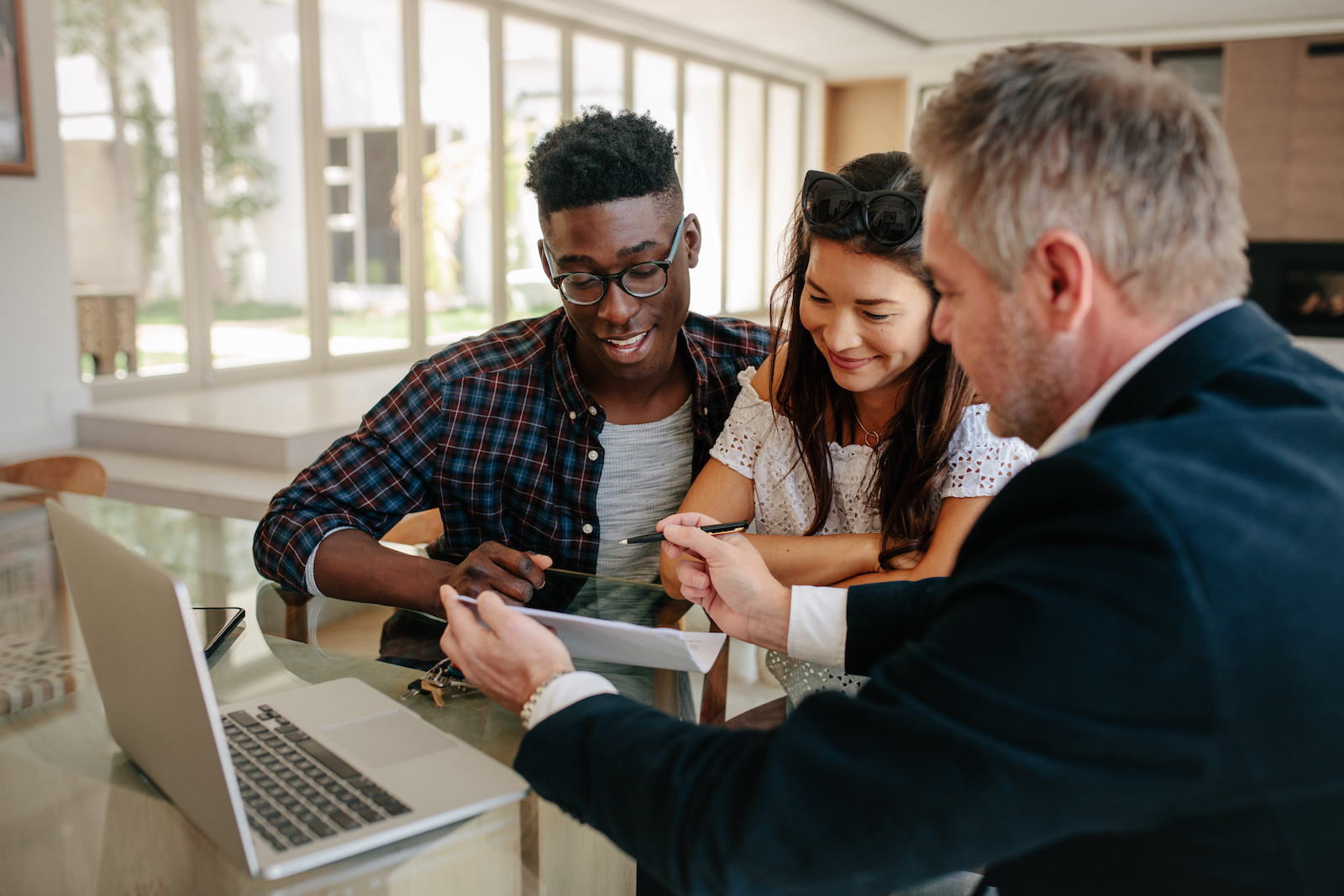 Male real estate agent offering to buy a new house to young couple during a meeting. Realtor presenting technical documentation to owner couple.